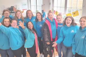 A group of women in bright blue hoodies smiling and waving